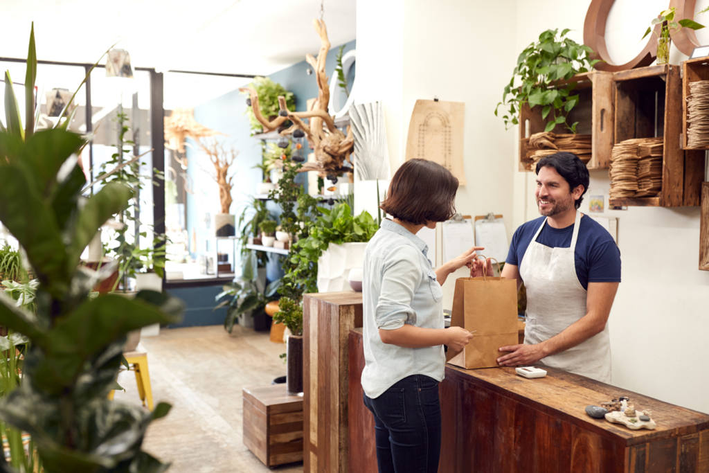 Male Sales Assistant In Florists Shop Serving Female Customer At Sales Desk