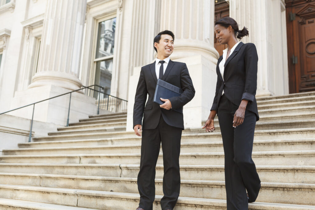 A well dressed man and woman legal professionals smiling as they as they walk down steps of a courthouse building.