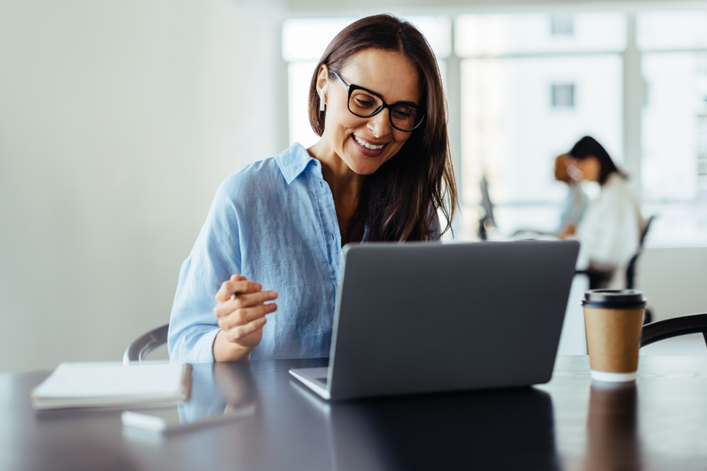 Woman with glasses happily typing on a laptop.