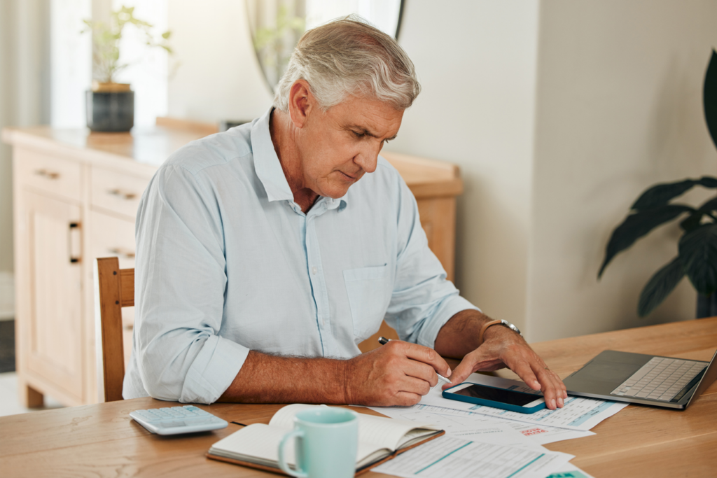 A senior man sitting at a desk in his home, focused on paperwork.